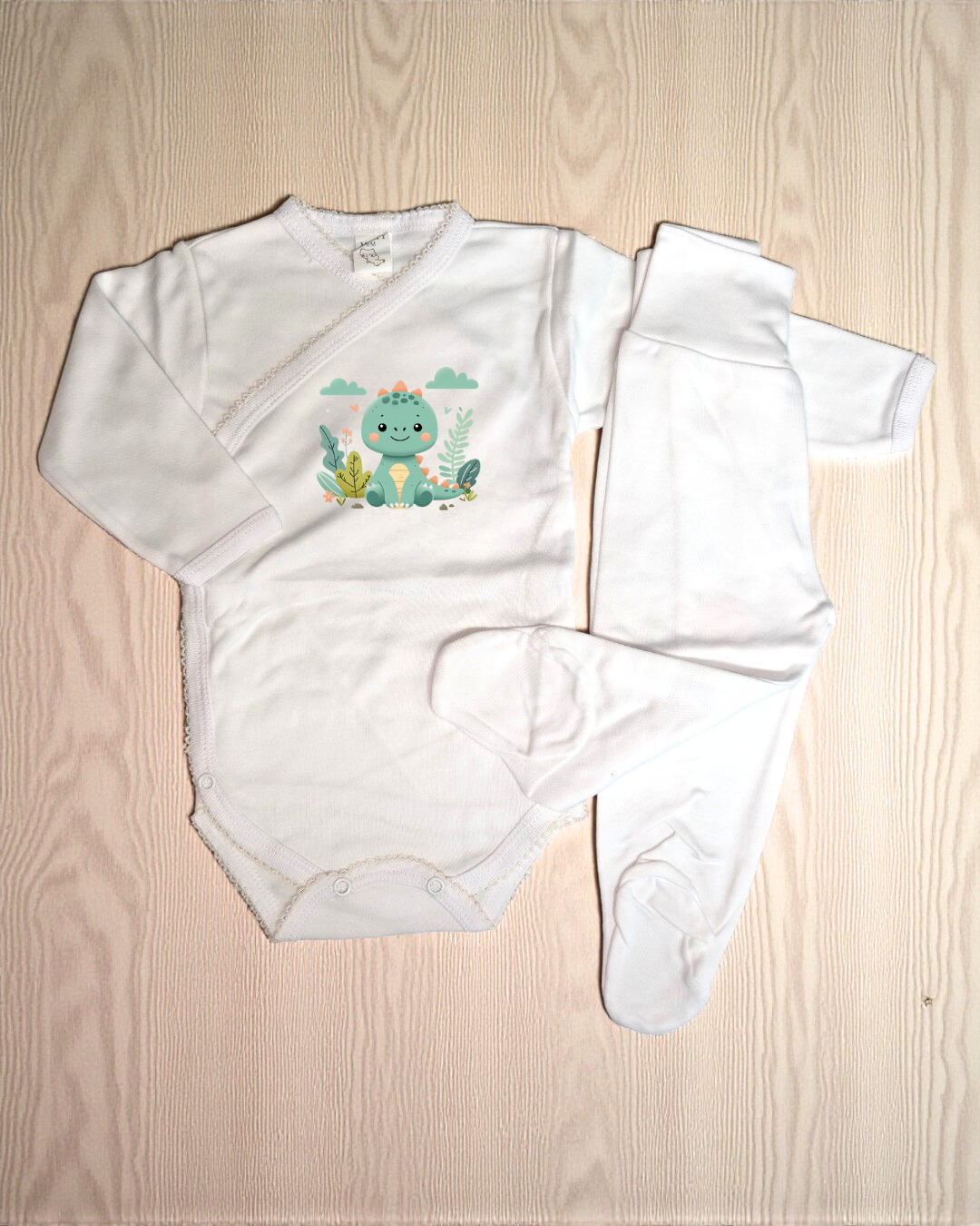 Conjunto de roupa de bebé branco com estampa de dinossauro azul e verde numa superfície de madeira clara