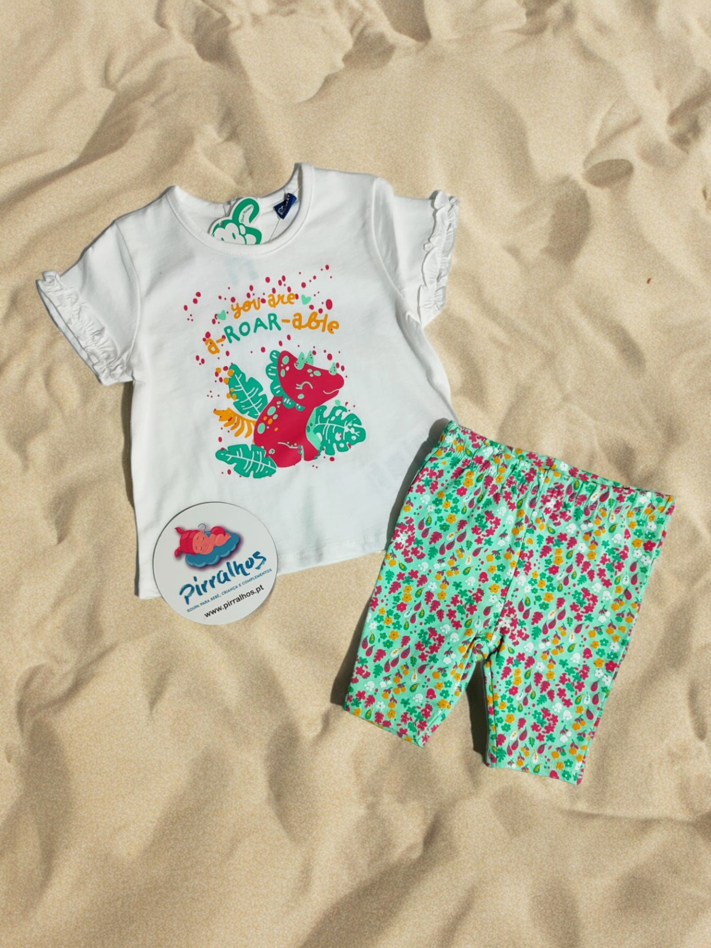 Conjunto roupa infantil com t-shirt branca e calções florais sobre areia