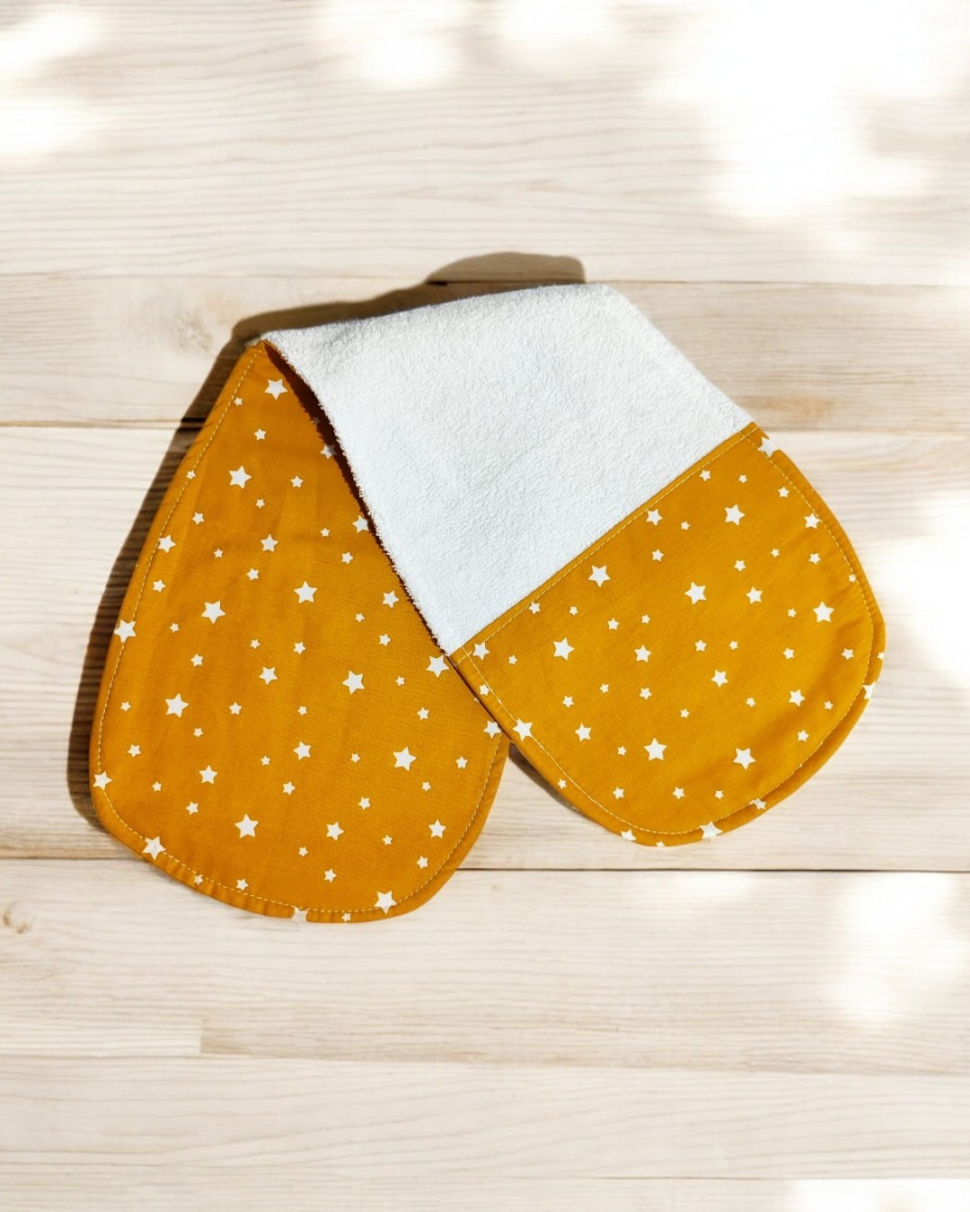 Pega de cozinha dupla amarelo mostarda com estrelas brancas em tecido e lado branco felpudo sobre madeira