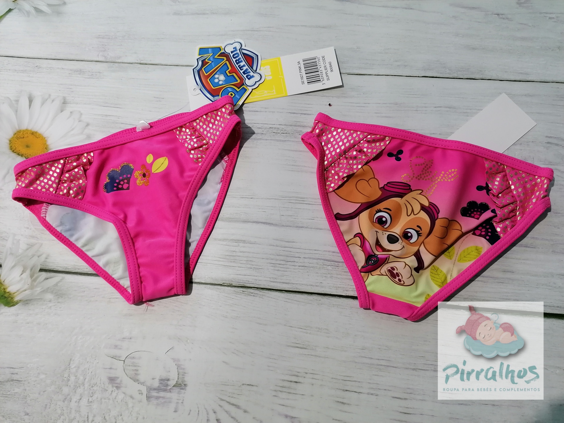 Biquinis infantis cor-de-rosa com personagem animado e padrões coloridos sobre superfície de madeira clara