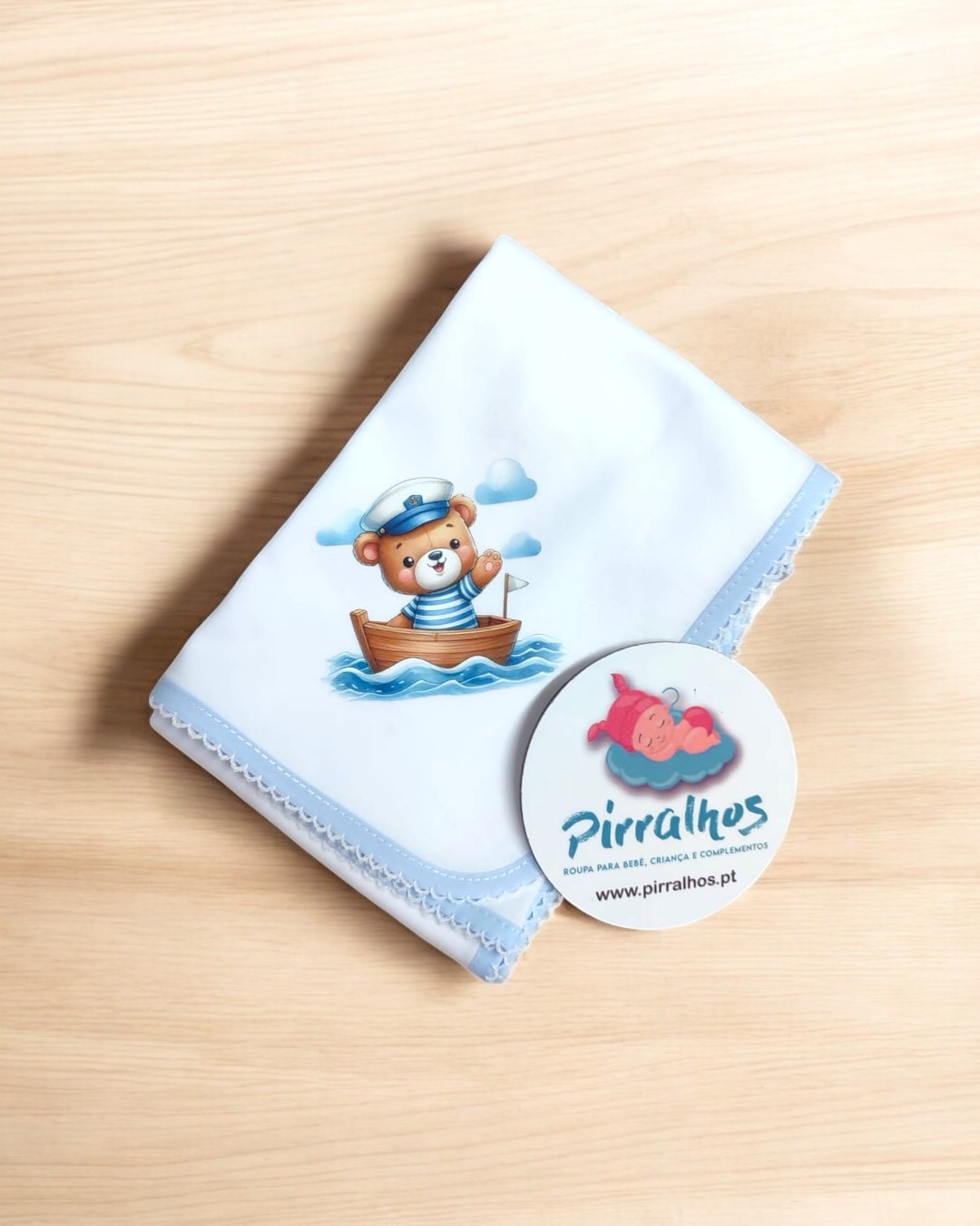 Fralda branca com urso marinheiro e etiqueta da marca Pirralhos