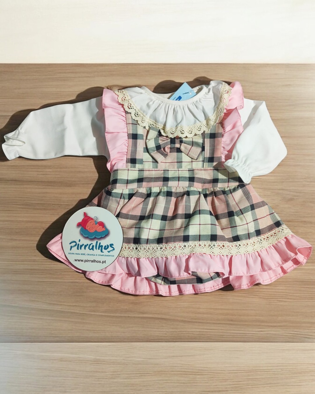 Vestido infantil às riscas com folhos rosa e blusa branca sobre madeira clara.