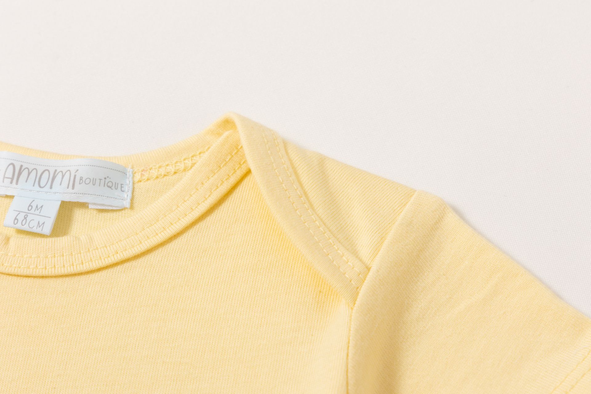 Peça de roupa amarela para bebé com etiqueta de tamanho e marca