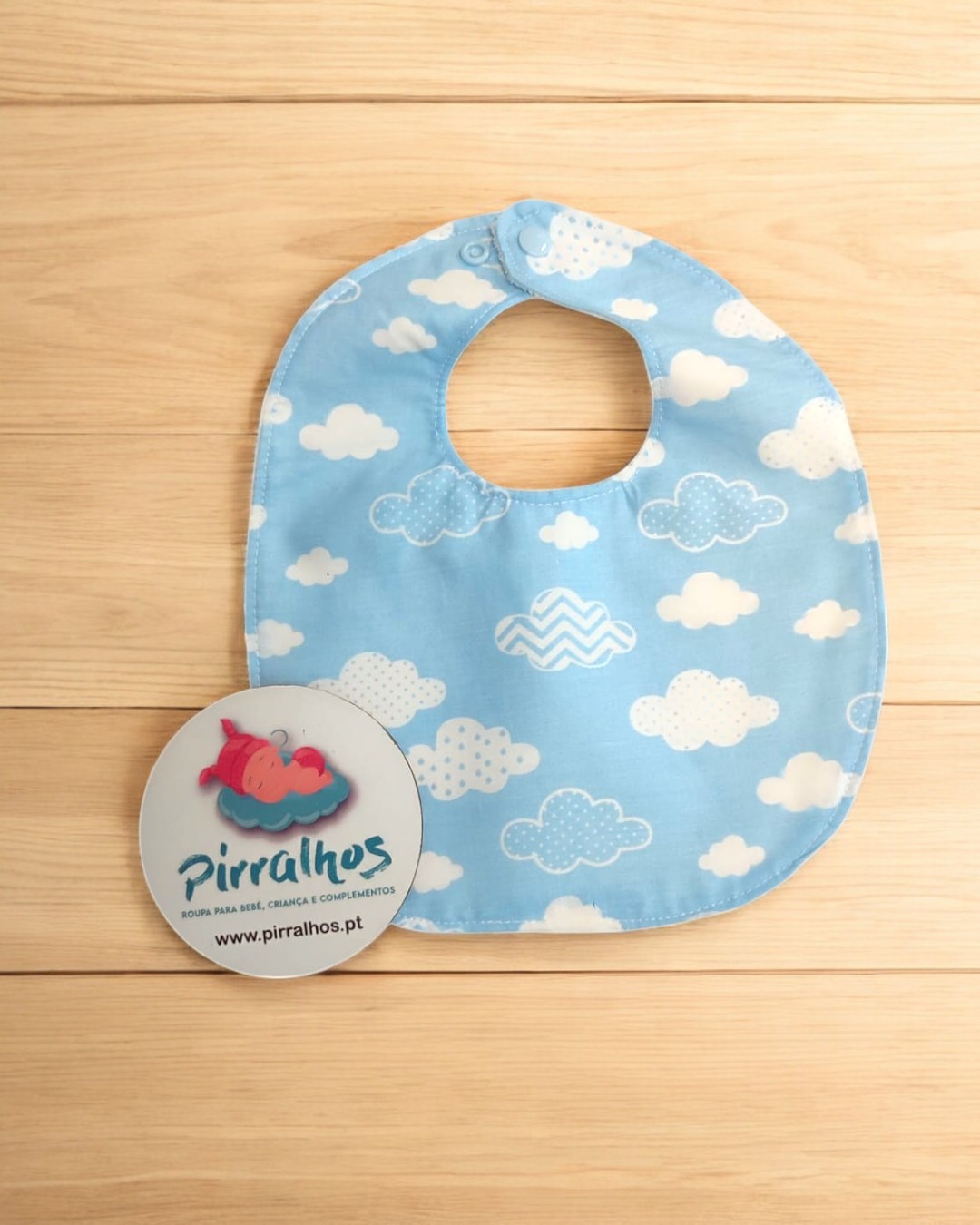Babete azul claro com padrão de nuvens e etiqueta redonda com logótipo