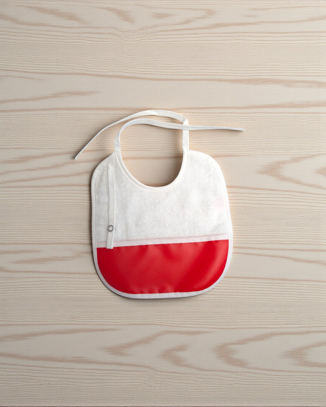 Babete de bebé branco e vermelho sobre mesa de madeira clara