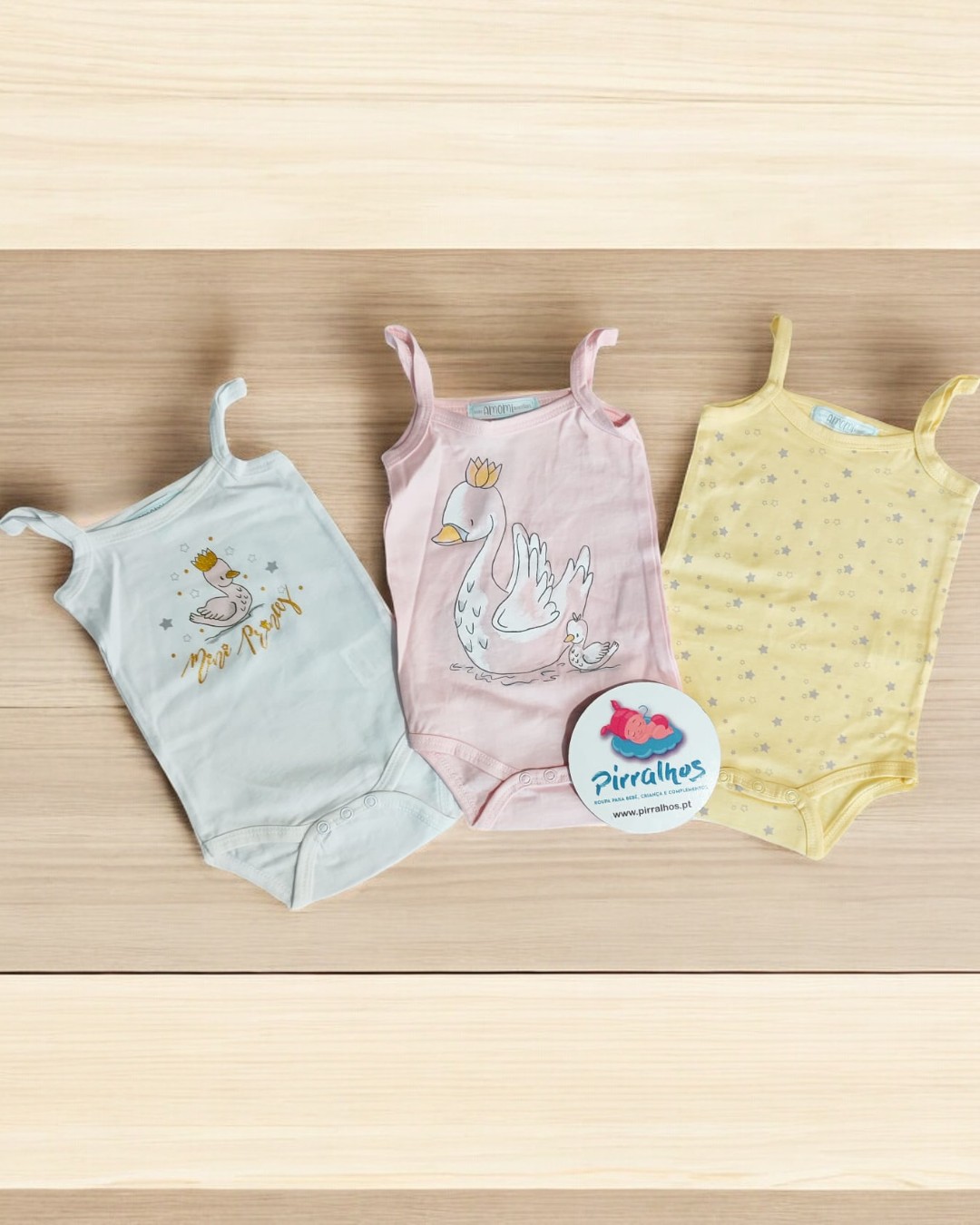 Três bodies de bebé com estampados de cisnes e estrelas sobre fundo claro.