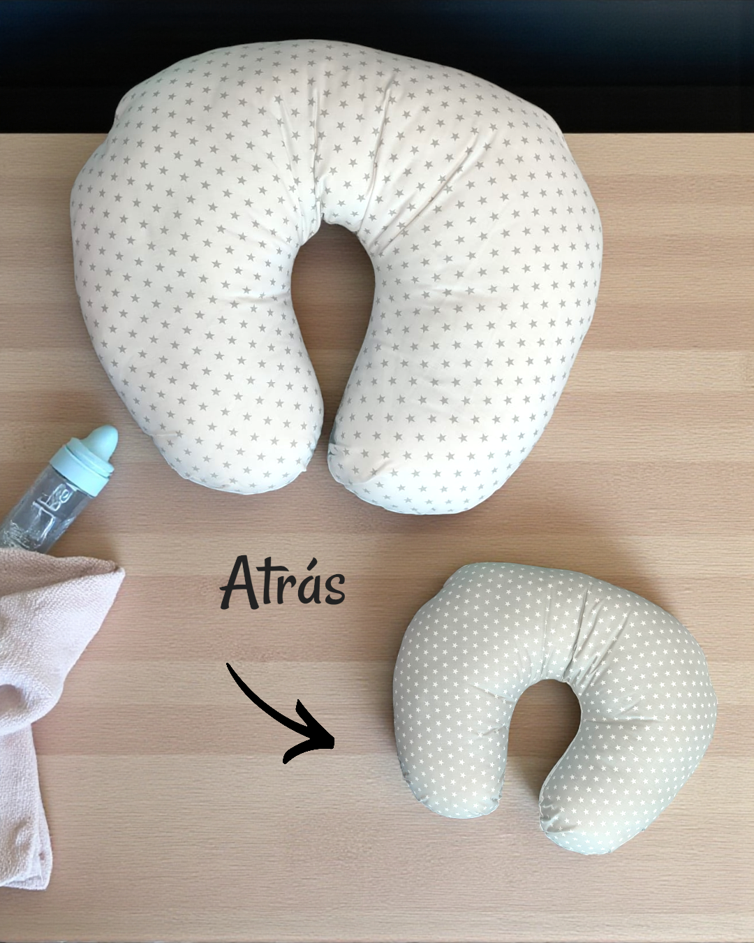 Três almofadas em U com padrões de estrelas e bolinhas, chupeta azul e pano rosa sobre mesa de madeira.