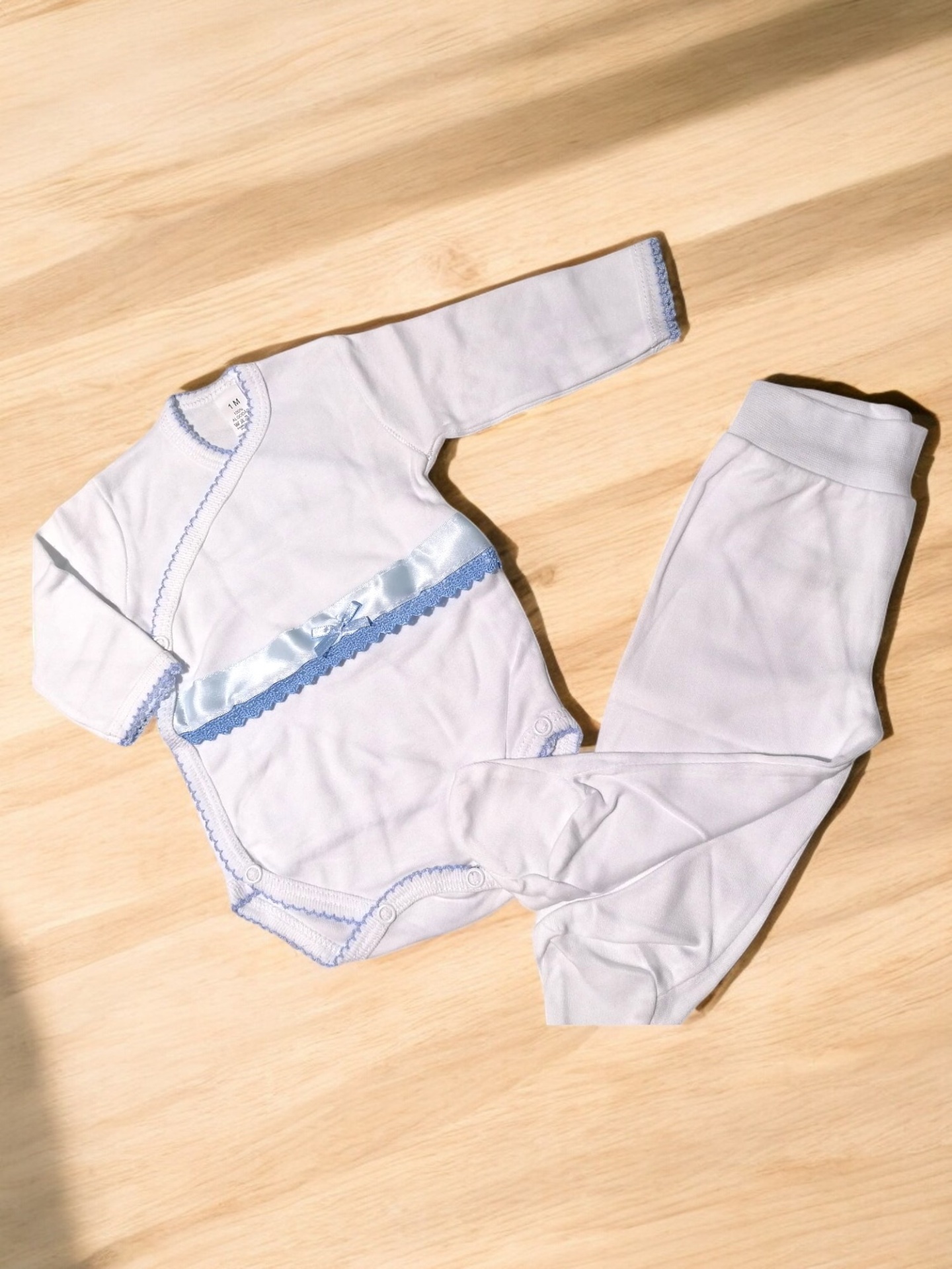 Conjunto de roupa para bebé branco com detalhes azuis sobre madeira clara