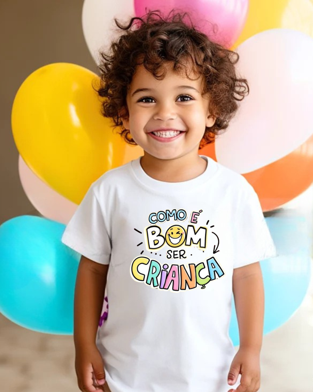 Criança sorridente com camisola branca e estampado colorido, balões ao fundo.