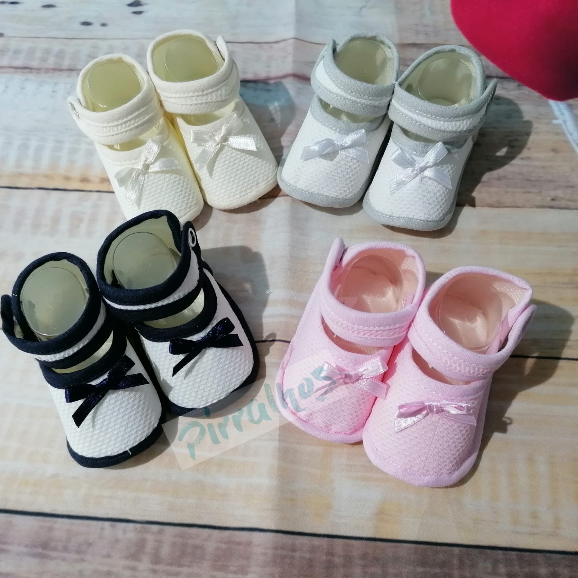 Quatro pares de sapatinhos de bebé em tecido coloridos com laços, sobre mesa de madeira clara