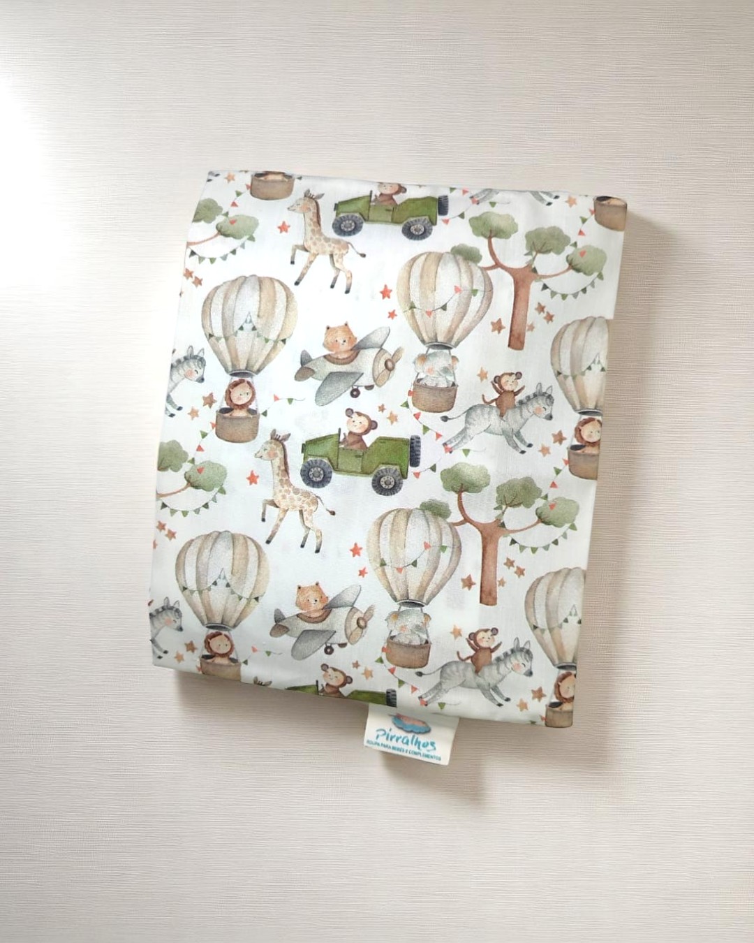 Fralda de pano com padrão infantil de balões, carros e animais em cores suaves.