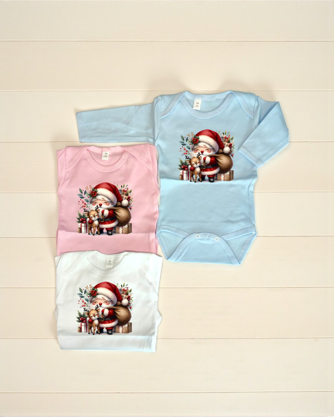 Três bodies de bebé com estampa de Pai Natal e rena, nas cores azul claro, rosa e branco