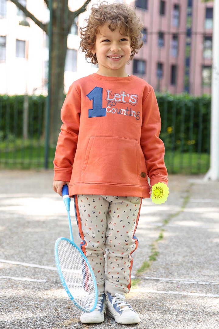 Criança sorridente com roupa desportiva e raquete de badminton ao ar livre