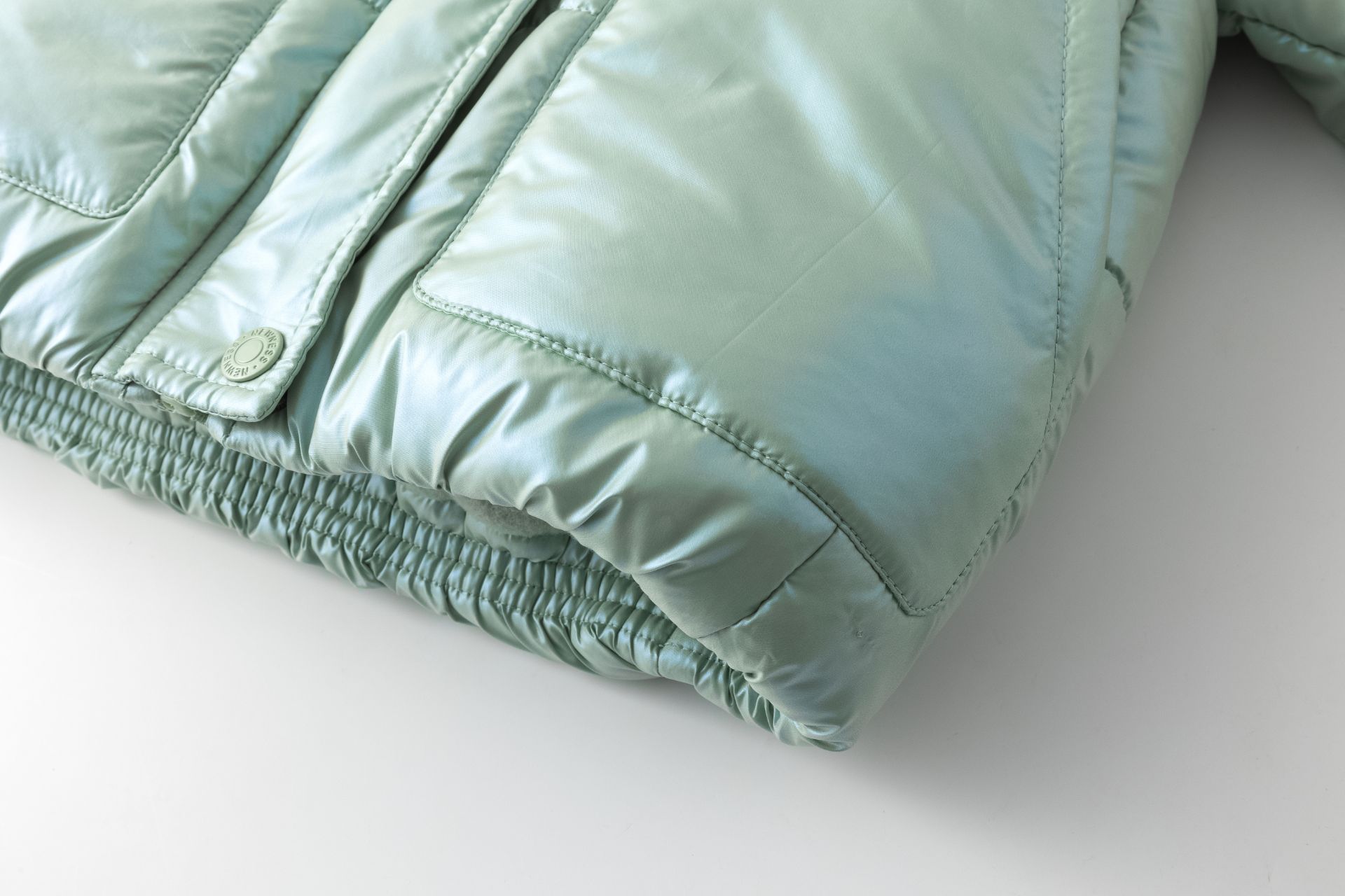 Casaco acolchoado verde claro com botão metálico e bainha elástica.