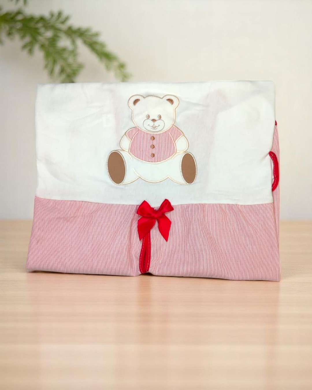 Produto têxtil dobrado com ursinho bordado e laço vermelho