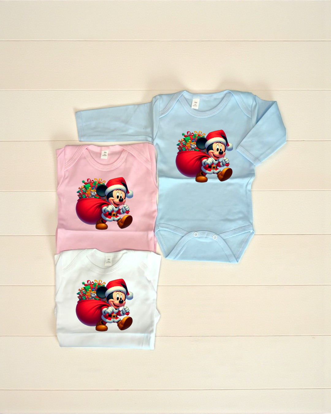 Três bodies de bebé com estampa de Mickey Pai Natal em cores azul, rosa e branco