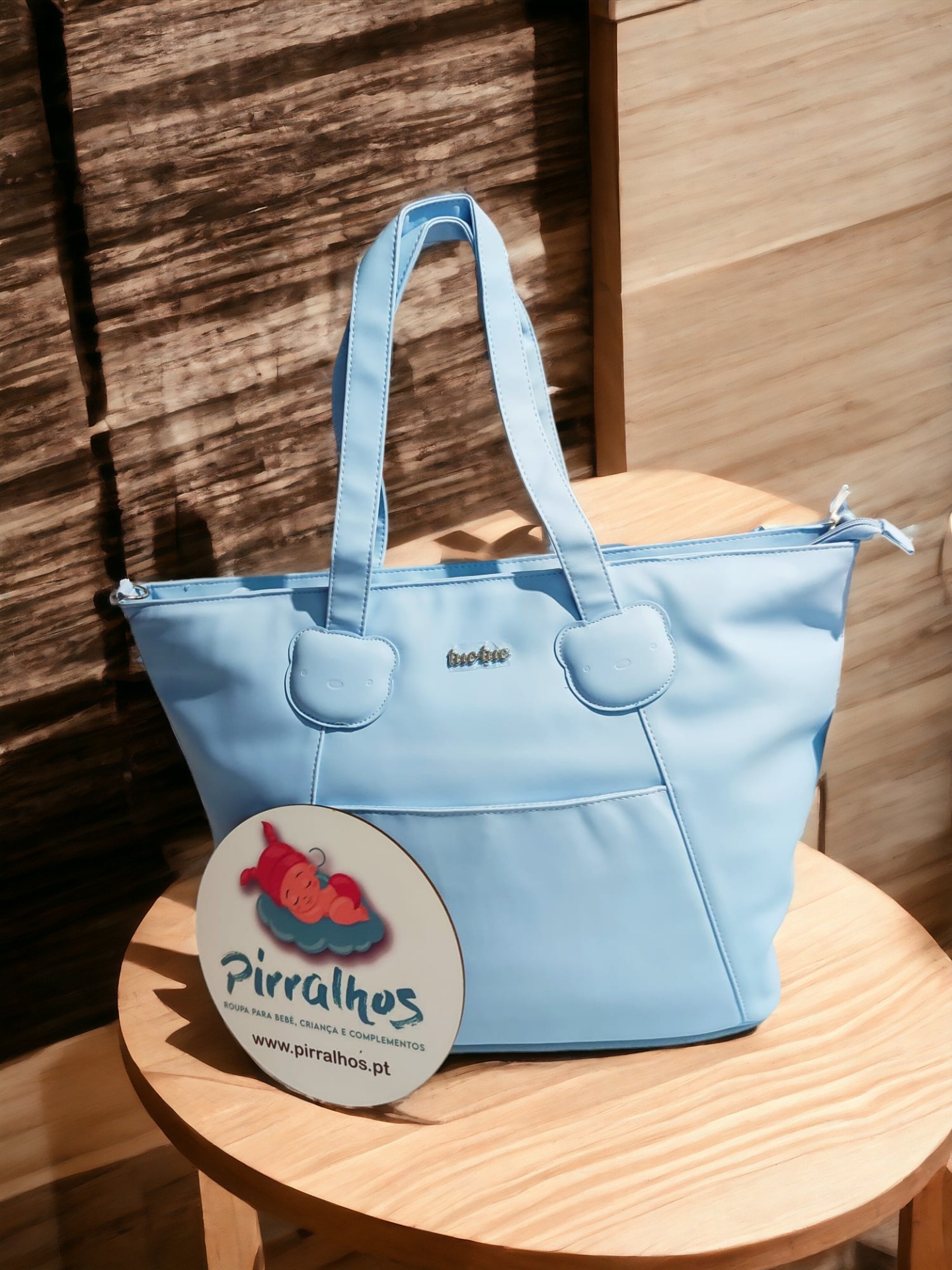 Mala de mão azul claro com alças e bolso frontal sobre cadeira de madeira clara