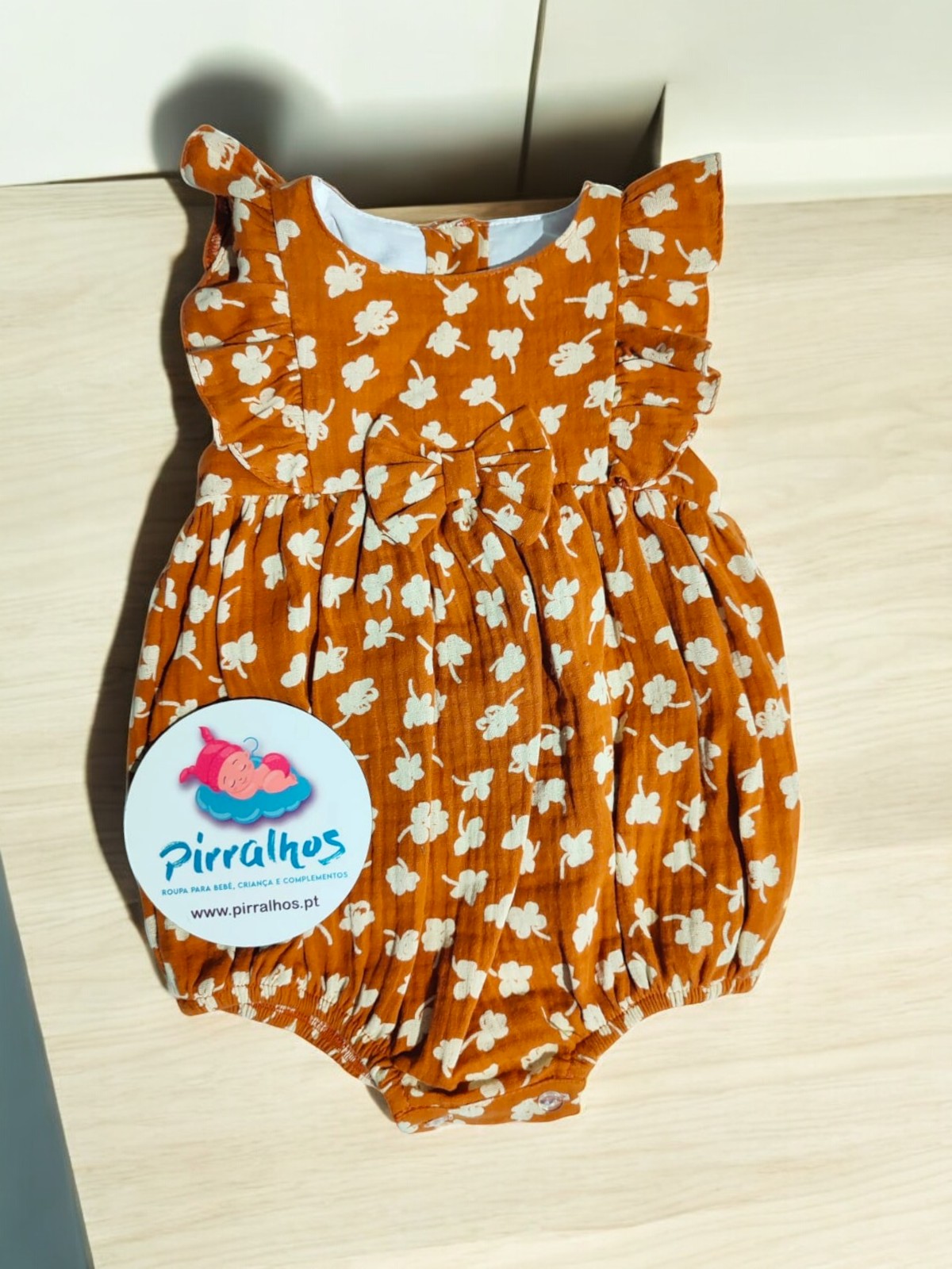 Body de bebé castanho com flores brancas e folhos, com etiqueta 'Pirralhos'