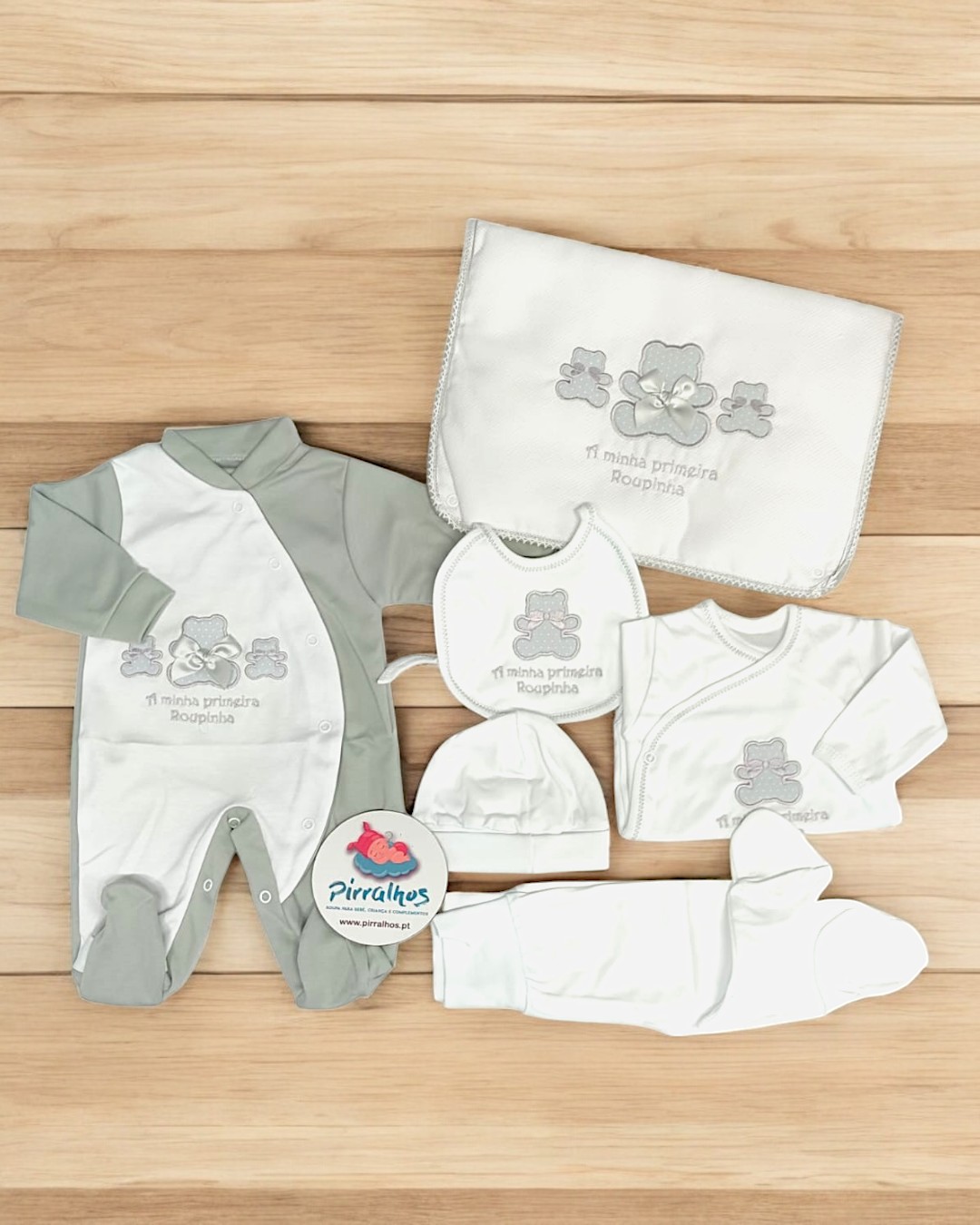 Conjunto de roupa de bebé branco e cinza com ursinhos bordados e manta, disposição em fundo de madeira