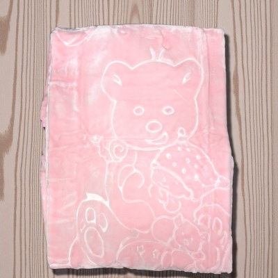 Cobertor rosa aveludado com padrão de ursinho em relevo sobre mesa de madeira clara