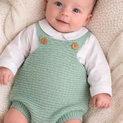 Bebé com macacão verde claro e camisa branca numa manta de malha creme