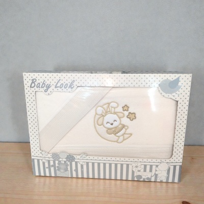 Conjunto branco para bebé com bordado de coelho na lua em embalagem decorada com bolinhas e desenhos infantis.