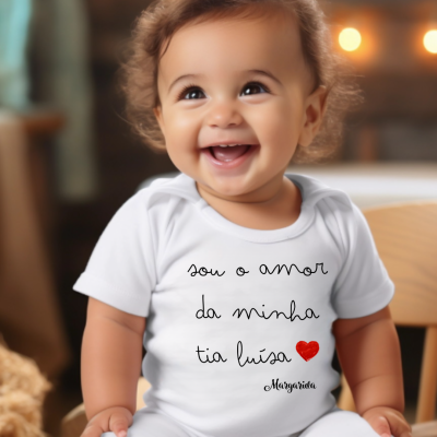 Bebé sorridente com body branco com texto em português e coração vermelho sentado em ambiente interior