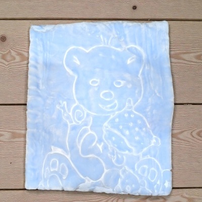 Manta azul clara com padrão de urso em relevo numa superfície de madeira.