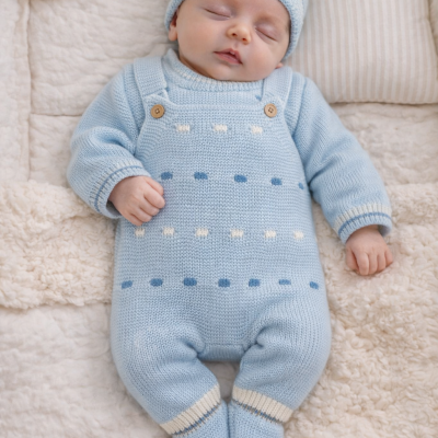 Bebé a dormir com macacão e gorro de malha azul-claro sobre manta felpuda bege