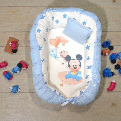 Ninho para bebé azul e branco com estampa do Mickey Mouse e almofada azul num chão de madeira com brinquedos.