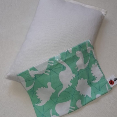 Travesseiro branco com fronha verde com padrão de dinossauros brancos.