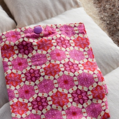Bolsa de tecido com padrão geométrico floral rosa e vermelho sobre almofadas brancas