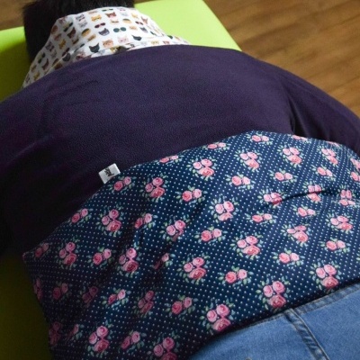 Homem deitado de bruços com camisa floral azul e rosa e calça de ganga azul