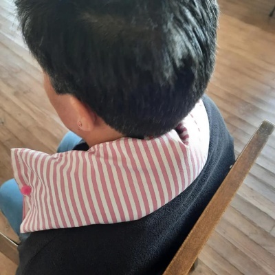 Pessoa com suporte de pescoço riscado vermelho e branco sentada numa cadeira de madeira