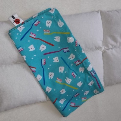 Almofada cinza com bolsa azul estampada com dentinhos e escovas de dentes