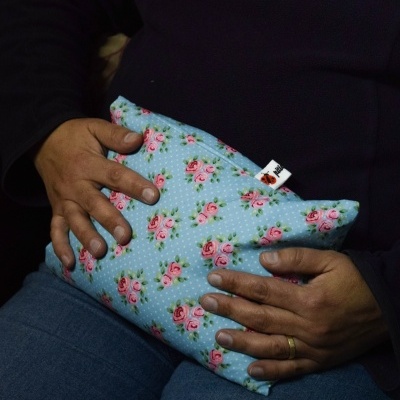 Almofada azul com padrão de rosas nas mãos de uma pessoa sentada.