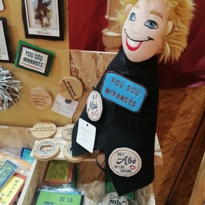 Boneco de pelúcia com capa preta e etiquetas de madeira e tecido ao redor