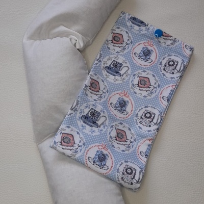 Almofada cinzenta clara e bolsa azul com padrão de portas, janelas e relógios sobre superfície branca