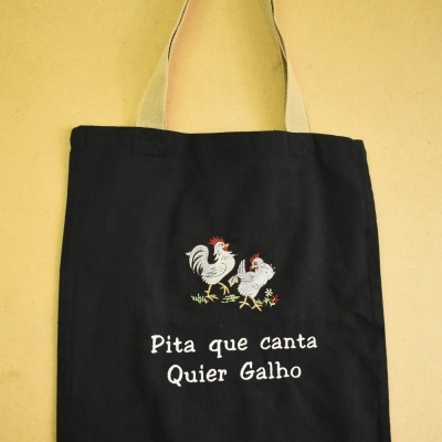 Mala preta com alças bege e bordado de galo e galinha com texto em branco