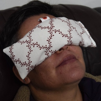 Almofada para os olhos branca com padrão de ramos vermelhos em pessoa sentada no sofá