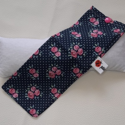 Almofada térmica com capa azul escura com padrão de rosas vermelhas e pontos brancos e botão rosa