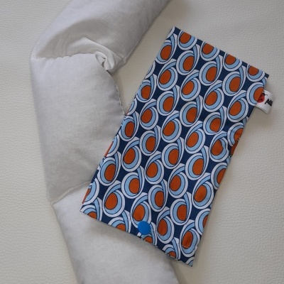 Três almofadas brancas e bolsa com padrão azul, branco e laranja numa superfície branca