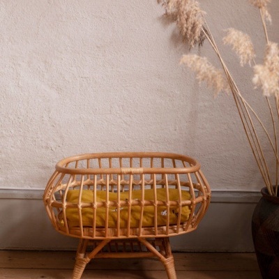 Berço de verga natural com almofada amarela junto a parede clara e vaso com plantas decorativas