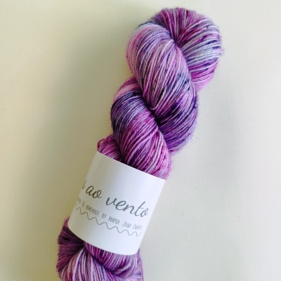 Novelo de lã artesanal em tons de lilás, rosa e roxo com etiqueta ao vento