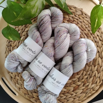 Três novelos de lã cinza com manchas coloridas sobre base trançada com folhagem ao redor