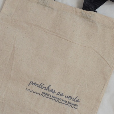 Saco de tecido bege com texto azul e alças pretas