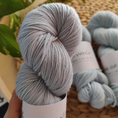 Novelo de lã cinzento claro com etiqueta branca numa mão, outros novelos ao fundo