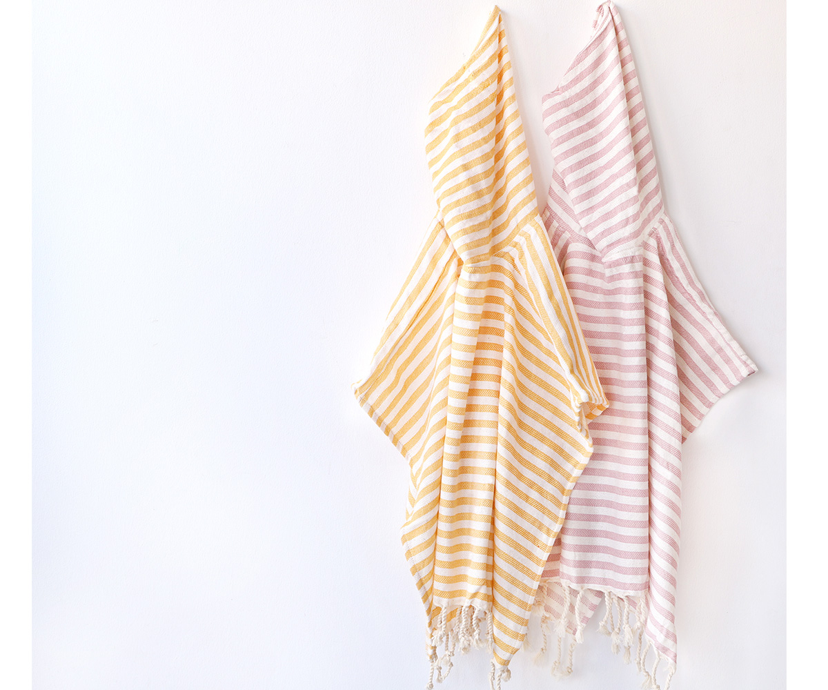 Duas toalhas com riscas, amarelas e rosa, penduradas numa parede branca