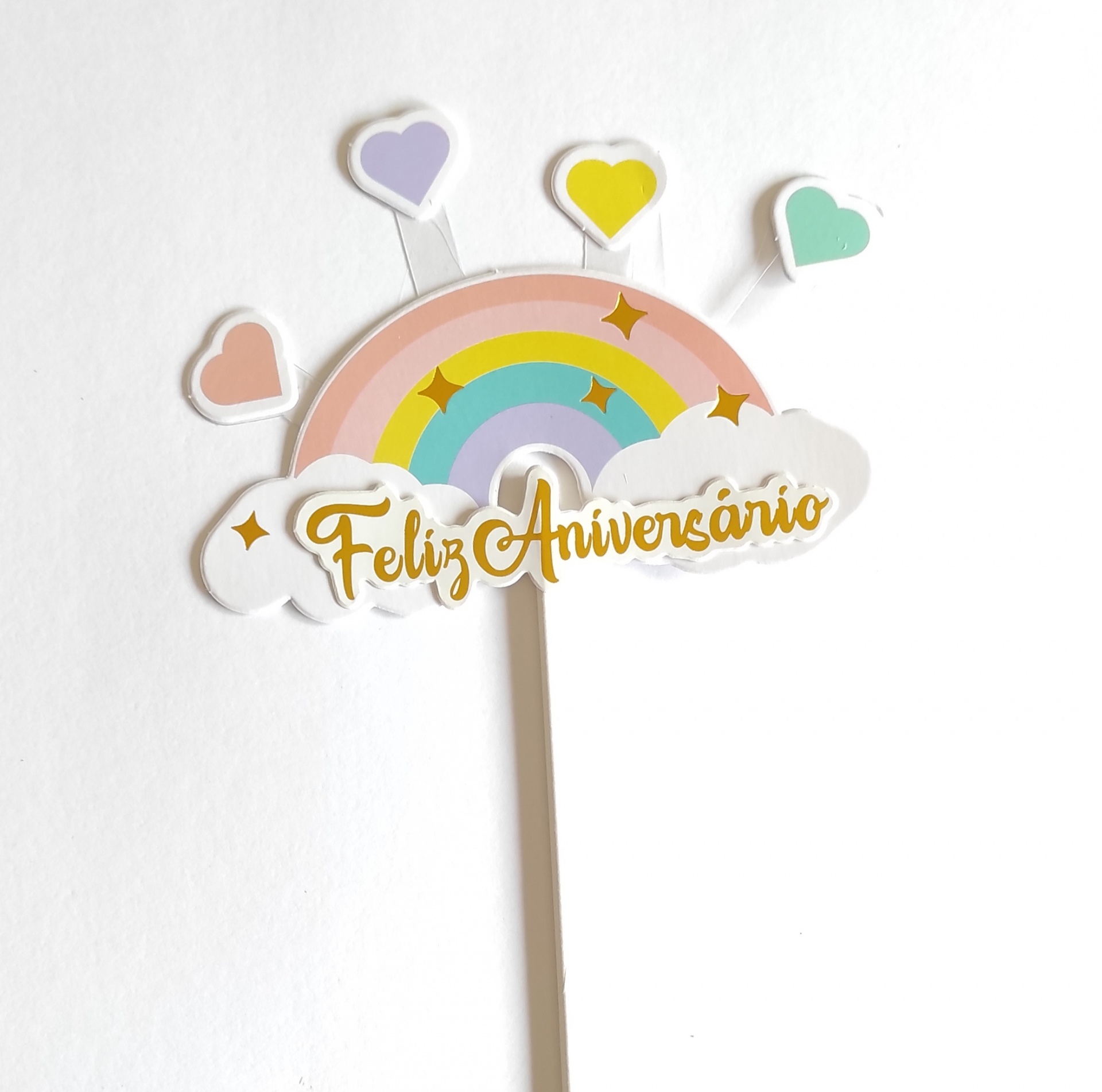 Topo de bolo decorativo arco-íris com a frase Feliz Aniversário e corações coloridos