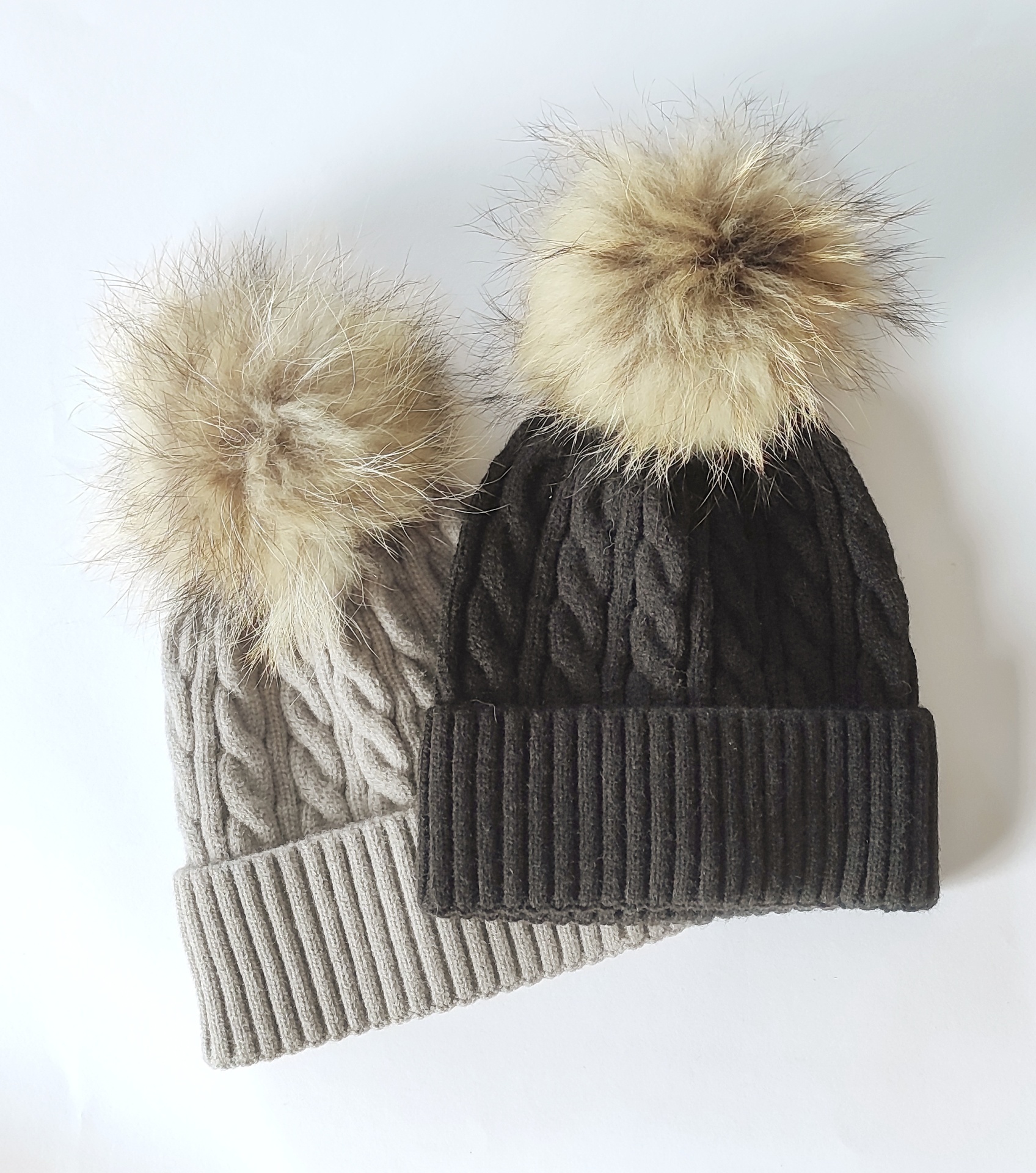 Dois gorros de malha com pompons peludos, um cinzento claro e outro castanho escuro